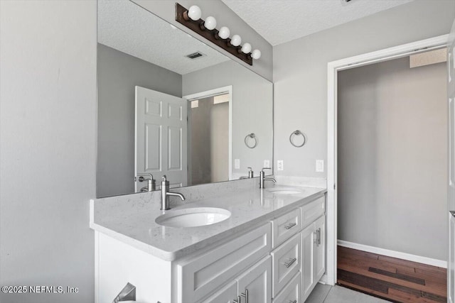 full bath featuring double vanity, a textured ceiling, baseboards, and a sink