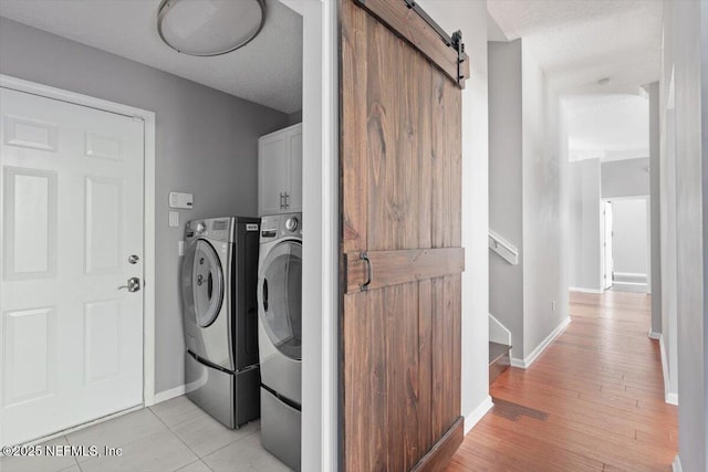 laundry area featuring cabinet space, a barn door, baseboards, a textured ceiling, and separate washer and dryer