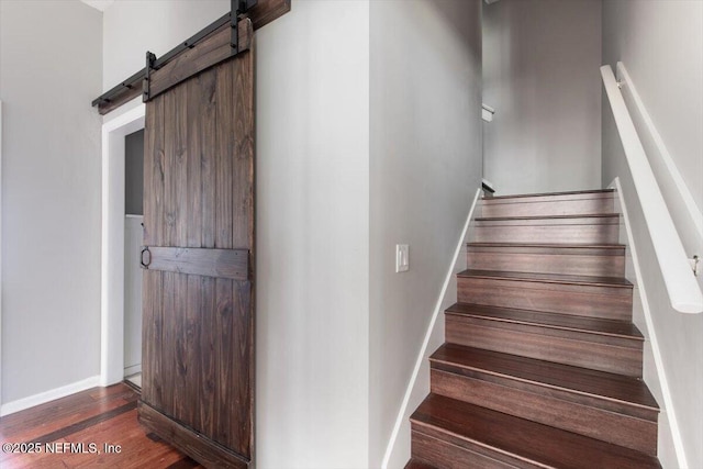 staircase featuring a barn door, baseboards, and wood finished floors