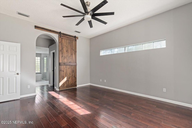 unfurnished room featuring a barn door, visible vents, ceiling fan, and dark wood-type flooring