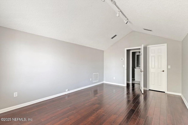 empty room featuring baseboards, visible vents, dark wood-style floors, vaulted ceiling, and a textured ceiling