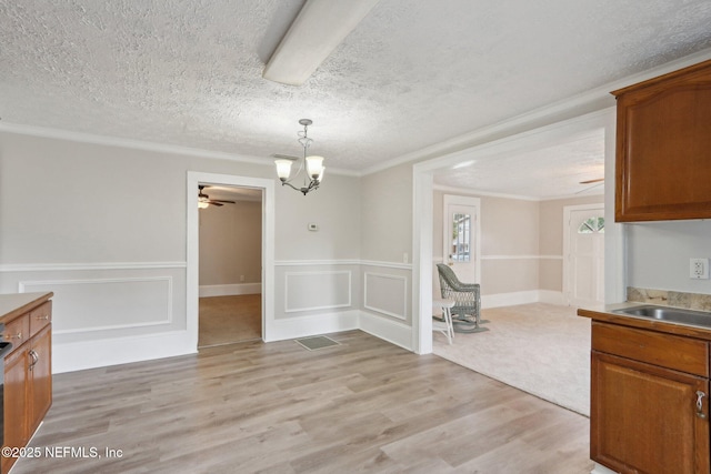 dining space featuring light wood finished floors, ornamental molding, a textured ceiling, and a wainscoted wall