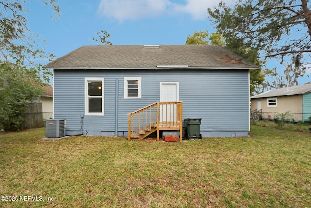 back of property featuring central AC, a shingled roof, a lawn, and fence