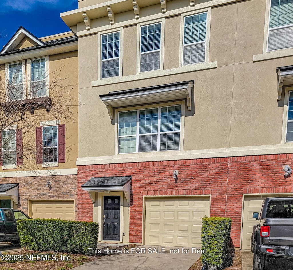 view of property with brick siding, stucco siding, and an attached garage