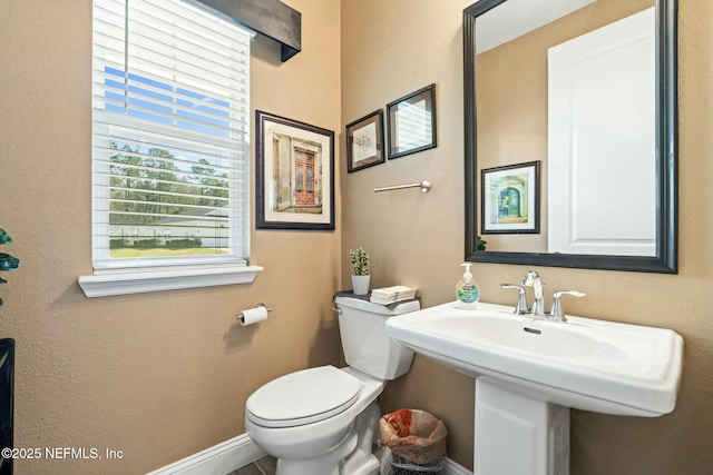 half bath featuring baseboards, a sink, and toilet