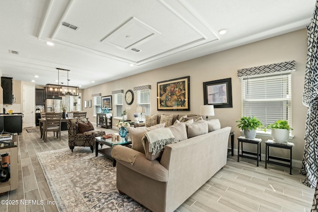 living room with baseboards, wood finish floors, visible vents, and an inviting chandelier