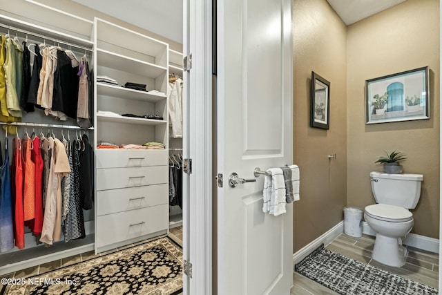 bathroom featuring wood tiled floor, baseboards, a spacious closet, and toilet