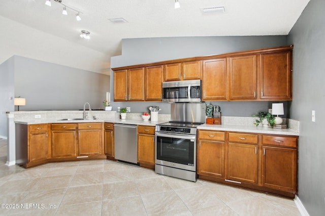 kitchen with brown cabinets, a sink, stainless steel appliances, light countertops, and vaulted ceiling