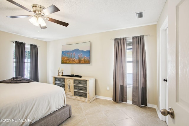 bedroom with light tile patterned floors, visible vents, a textured ceiling, and baseboards