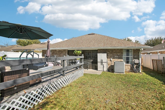 back of house with brick siding, a shingled roof, cooling unit, a yard, and a fenced backyard