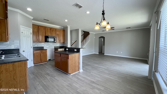 kitchen featuring arched walkways, brown cabinets, visible vents, light wood-style flooring, and black microwave