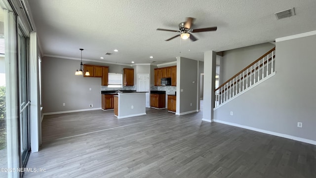 unfurnished living room with ceiling fan, dark wood-type flooring, visible vents, baseboards, and ornamental molding