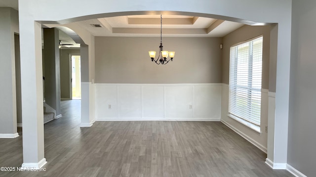 unfurnished dining area with visible vents, arched walkways, a raised ceiling, wood finished floors, and ceiling fan with notable chandelier