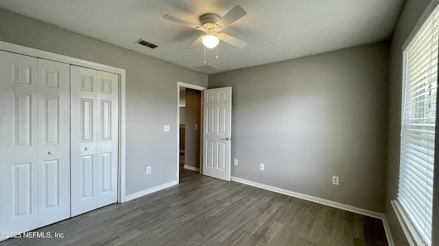 unfurnished bedroom with a textured ceiling, wood finished floors, visible vents, baseboards, and a closet