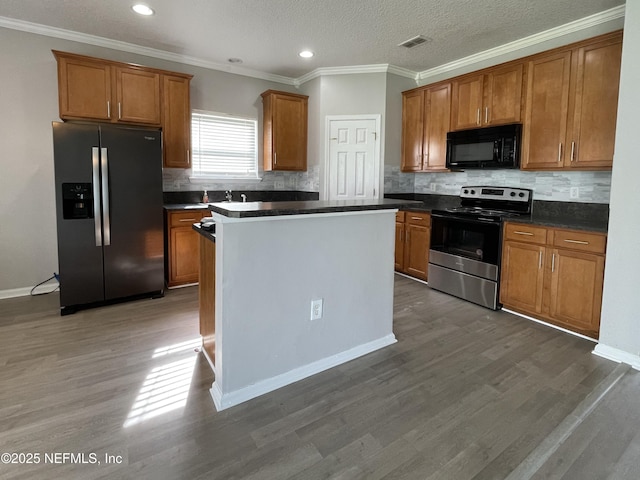 kitchen with dark countertops, visible vents, appliances with stainless steel finishes, brown cabinetry, and dark wood-type flooring