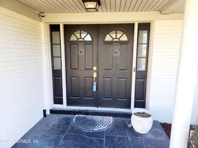 view of exterior entry with a porch and brick siding