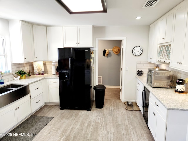 kitchen featuring a sink, black fridge with ice dispenser, visible vents, white cabinetry, and light wood-type flooring