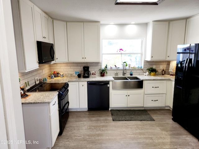 kitchen featuring black appliances, decorative backsplash, light wood-style floors, and a sink