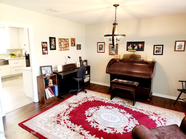 office space with visible vents, a notable chandelier, baseboards, and wood finished floors