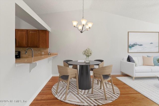 dining room featuring light wood-style flooring, baseboards, an inviting chandelier, and vaulted ceiling