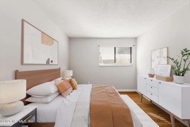 bedroom featuring baseboards, a textured ceiling, and wood finished floors