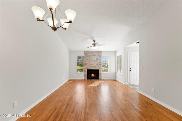 unfurnished living room featuring ceiling fan with notable chandelier, a fireplace, light wood-style floors, and a textured ceiling