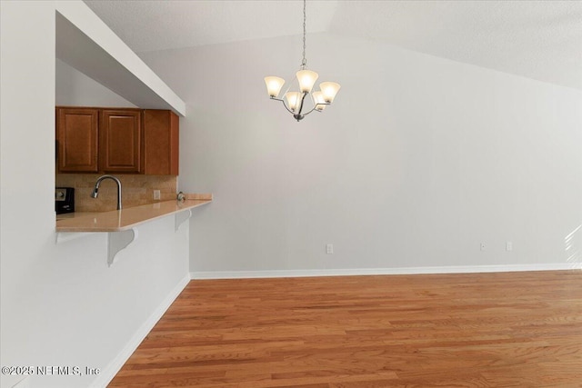 unfurnished dining area with a notable chandelier, lofted ceiling, light wood-type flooring, and baseboards