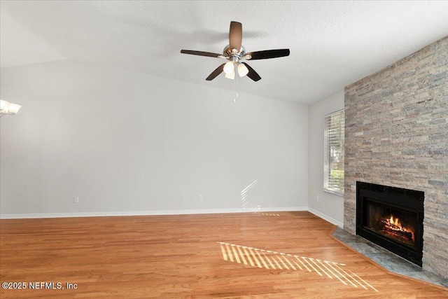 unfurnished living room with light wood-style flooring, a textured ceiling, baseboards, a stone fireplace, and lofted ceiling