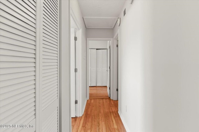 corridor featuring attic access, visible vents, and light wood finished floors