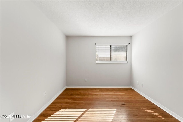 spare room with wood finished floors, baseboards, and a textured ceiling