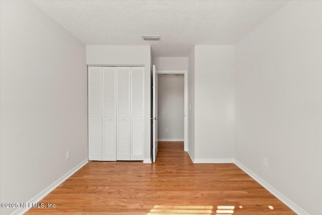 unfurnished bedroom with visible vents, baseboards, light wood-style floors, a closet, and a textured ceiling