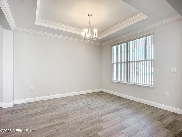 unfurnished room featuring a tray ceiling, crown molding, a notable chandelier, light wood finished floors, and baseboards