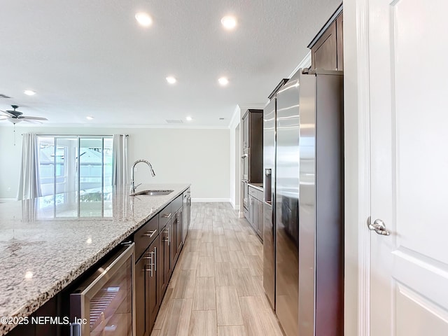 kitchen with light stone counters, beverage cooler, a sink, dark brown cabinets, and stainless steel refrigerator with ice dispenser