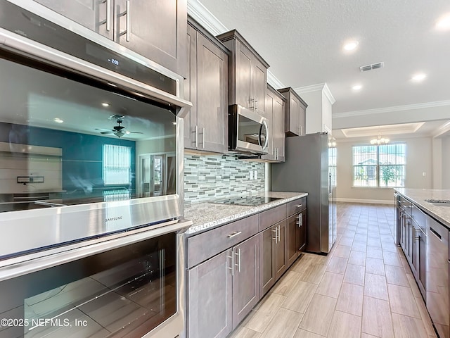 kitchen featuring dark brown cabinetry, visible vents, light stone counters, stainless steel appliances, and backsplash