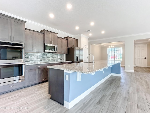 kitchen with stainless steel appliances, a breakfast bar, a sink, visible vents, and backsplash