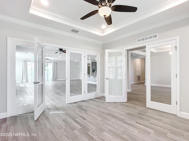 unfurnished room with light wood-style flooring, visible vents, a raised ceiling, and french doors