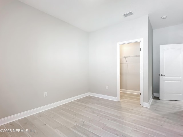 unfurnished bedroom with baseboards, visible vents, a walk in closet, light wood-type flooring, and a closet