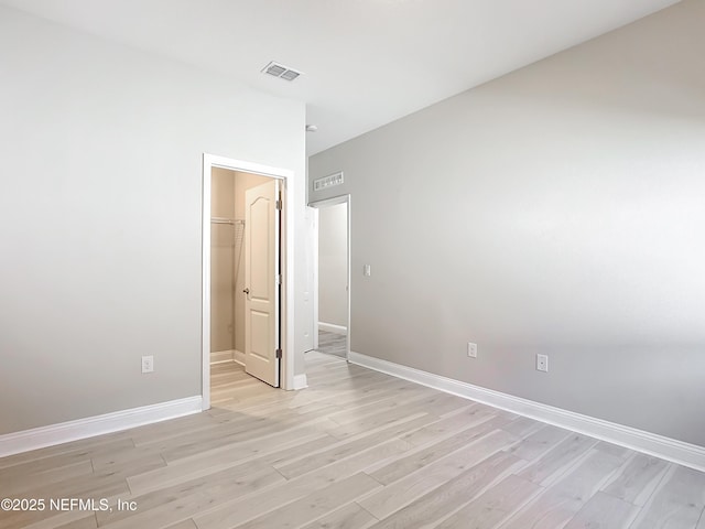 unfurnished bedroom featuring visible vents, light wood-style flooring, baseboards, and a spacious closet