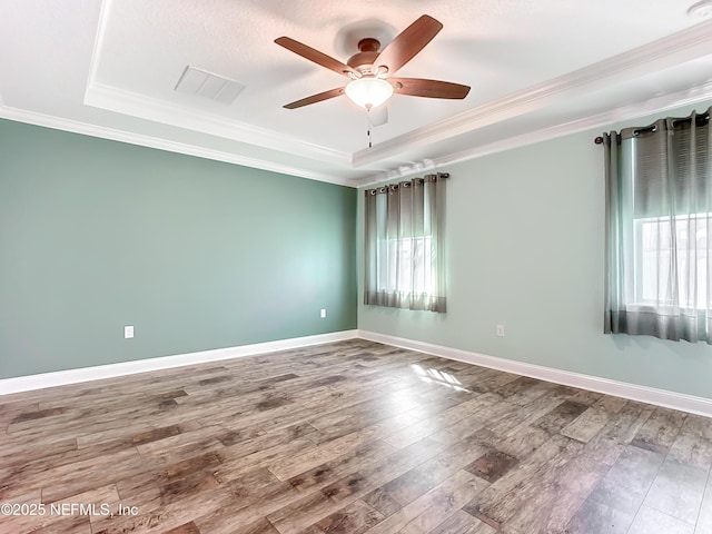 empty room featuring a tray ceiling, crown molding, visible vents, wood finished floors, and baseboards