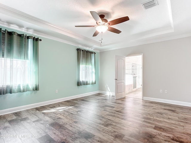 unfurnished room featuring ceiling fan, wood finished floors, visible vents, a tray ceiling, and crown molding