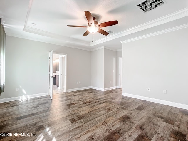 spare room with baseboards, visible vents, a tray ceiling, and wood finished floors