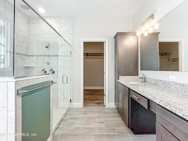 bathroom with a walk in closet, baseboards, a shower stall, and vanity