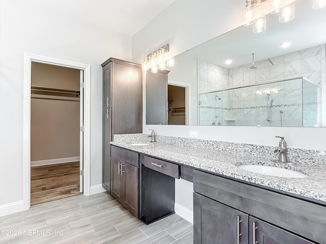 full bath featuring double vanity, a stall shower, a walk in closet, and a sink