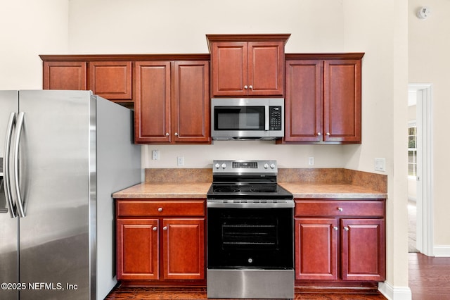 kitchen featuring reddish brown cabinets, dark wood-style floors, light countertops, appliances with stainless steel finishes, and baseboards