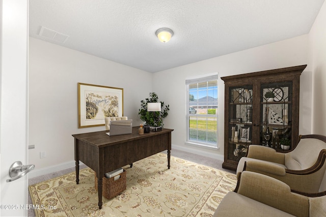 office space featuring a textured ceiling, carpet floors, visible vents, and baseboards