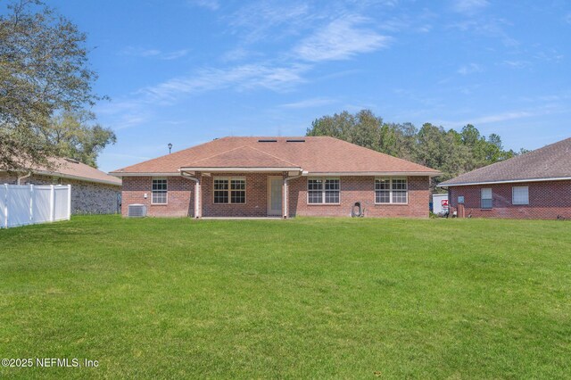 rear view of house featuring roof with shingles, fence, a lawn, and brick siding