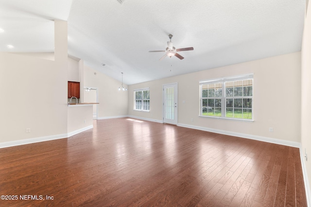 unfurnished living room with vaulted ceiling, ceiling fan with notable chandelier, wood-type flooring, and plenty of natural light