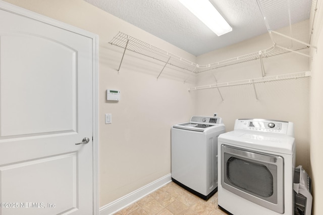 clothes washing area with a textured ceiling, laundry area, baseboards, and washer and dryer