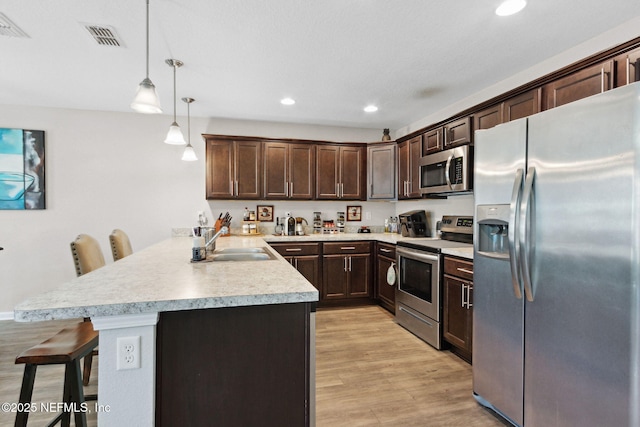 kitchen featuring a breakfast bar area, a peninsula, stainless steel appliances, dark brown cabinets, and a sink