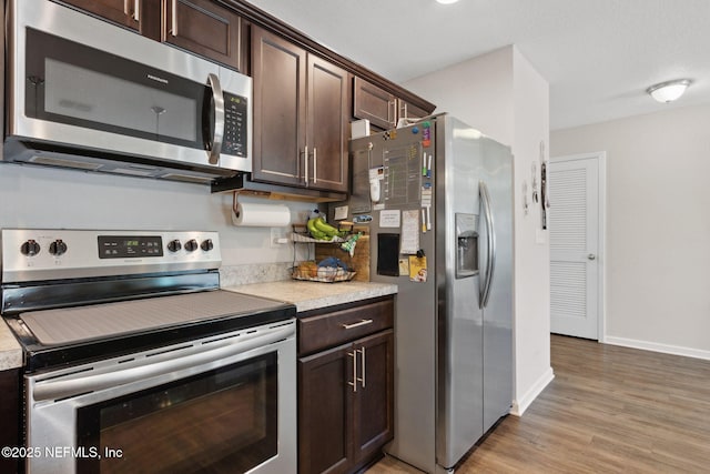 kitchen with light wood finished floors, stainless steel appliances, light countertops, dark brown cabinetry, and baseboards